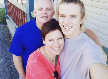 A selfie of the author, a white woman with short hair wearing a pink tee, with her son and husband