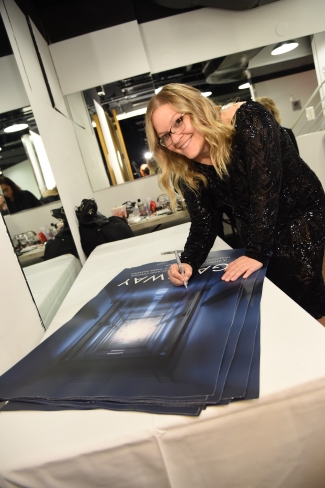 Jen Wysong, wearing a sparkly black dress, signing a movie poster
