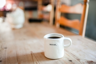 A white coffee mug that says "Begin" sits on a wooden table