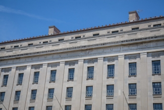 The United States Department of Justice, a large grey stone building against a blue sky. Photo by Tony Webster