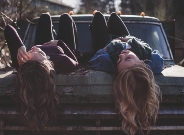 Two teen girls laying down and laughing on the hood of a truck