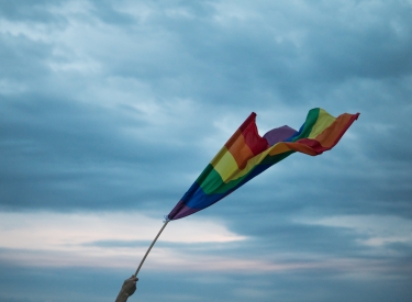 A hand lifting a Pride flag toward the sky. Image courtesy of Yannis Papanastasopoulos