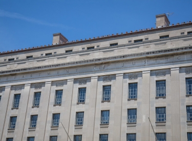 The United States Department of Justice, a large grey stone building against a blue sky. Photo by Tony Webster