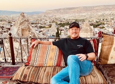 Chad smiling and lounging on an outdoor patio with a mountain view