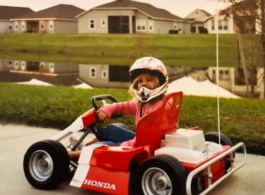 A childhood photo of the author's daughter, smiling in a red and white go cart