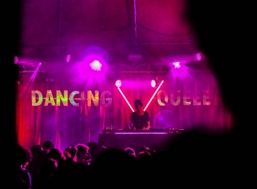 A DJ spins under pink and red lights at a dance party. Unsplash image via Juliette F