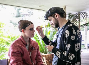 An actor has his face painted by a makeup artist on the set of Hide Your Crazy