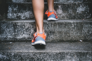 A white woman's feet, wearing orange and grey sneakers, walking up concrete stairs