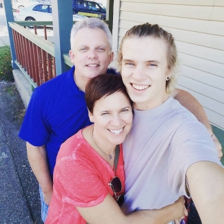 A selfie of the author, a white woman with short hair wearing a pink tee, with her son and husband