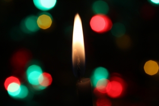A candle wick on a black background, with red, green, and gold lights